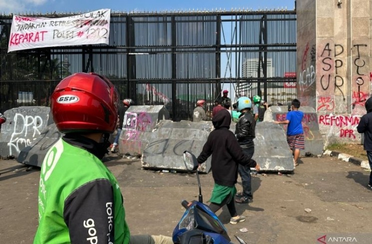 Sejumlah warga, termasuk seorang pengemudi ojek online (kiri), sengaja memberhentikan kendaraannya untuk melihat kondisi pascaunjuk rasa di depan gerbang utama Gedung DPR atau kompleks Gedung Parlemen, Senayan, Jakarta, Sabtu (30/8/2025). ANTARA/Rio Feisal
